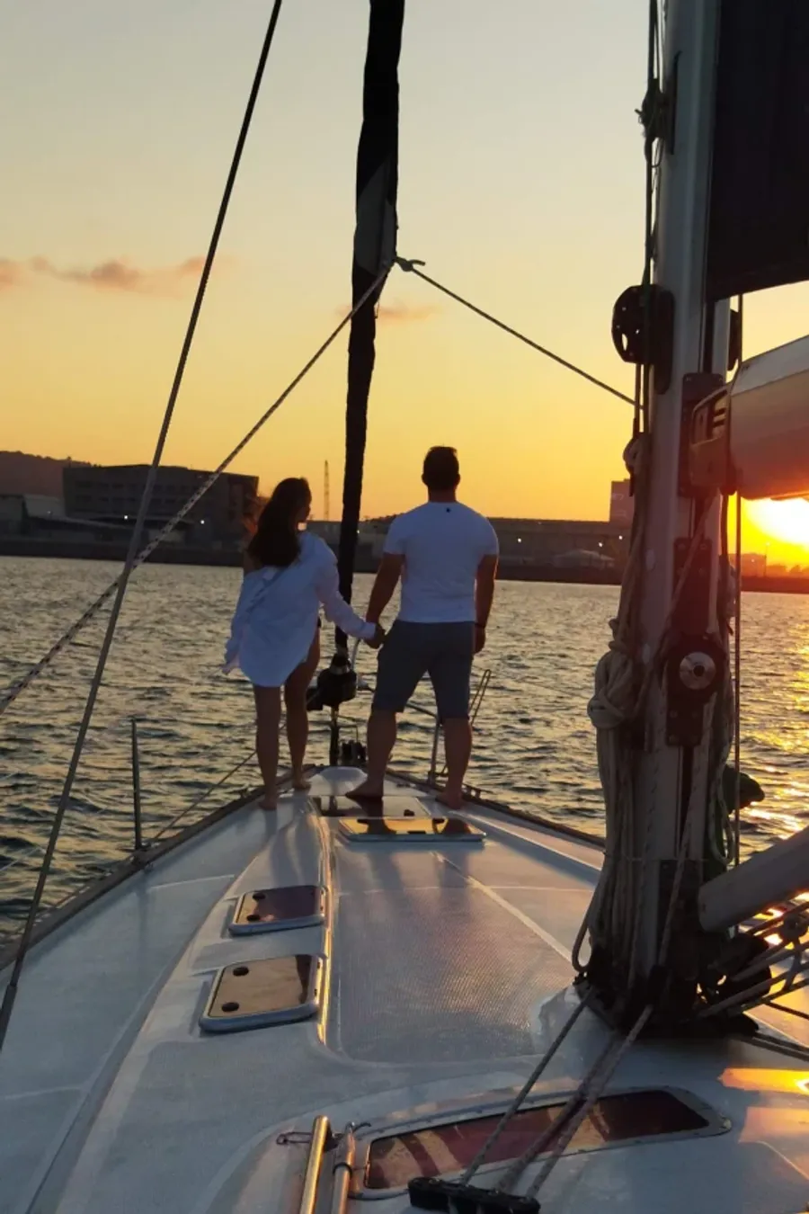 זוג מחזיק ידיים על חרטום היאכטה מול שקיעה בחיפה