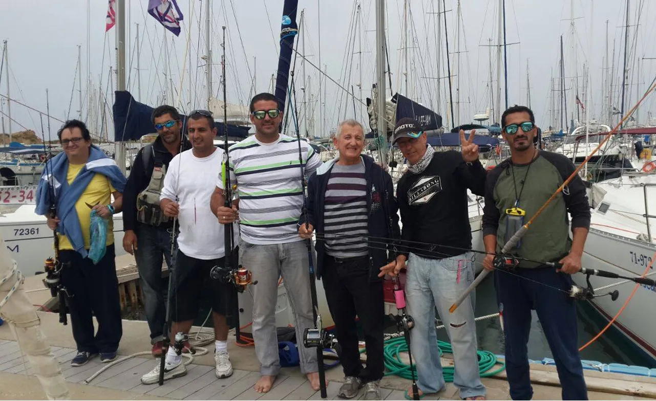 קבוצת דייגים עם חכות עומדים על המזח במרינה בהרצליה