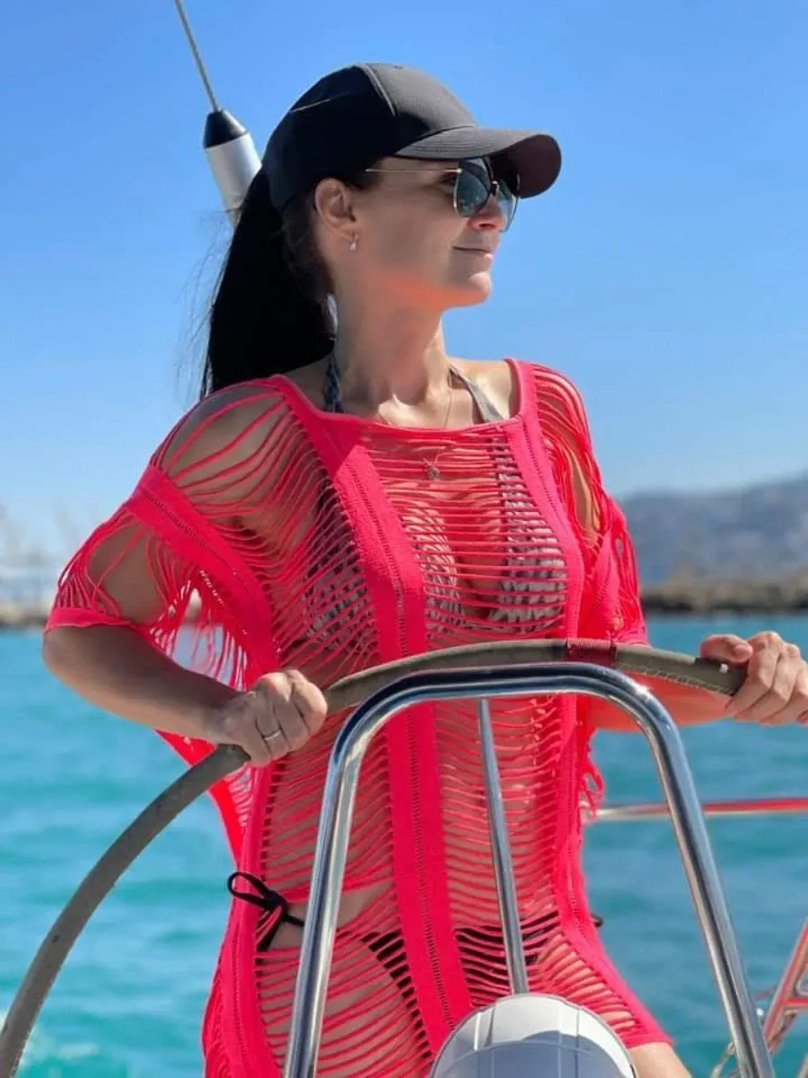 בחורה לבושה בבגד ים בצבע אדום אוחזת בהגה של יאכטה